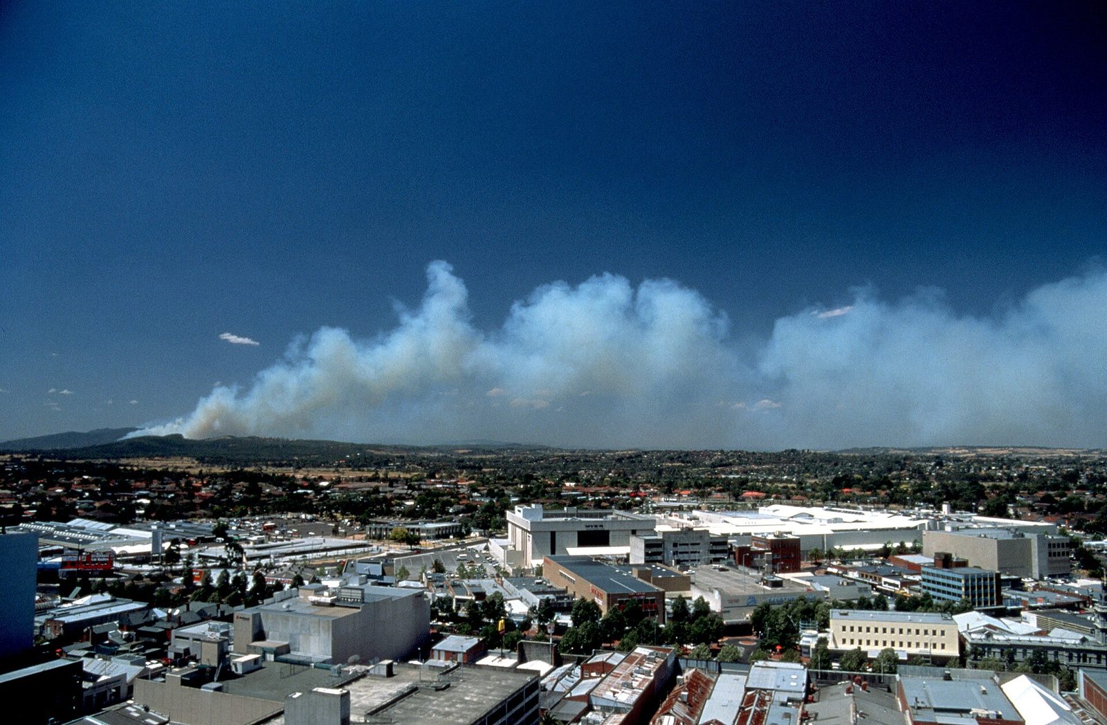 Distant bushfire smoke rising in columns over forested Australian hills